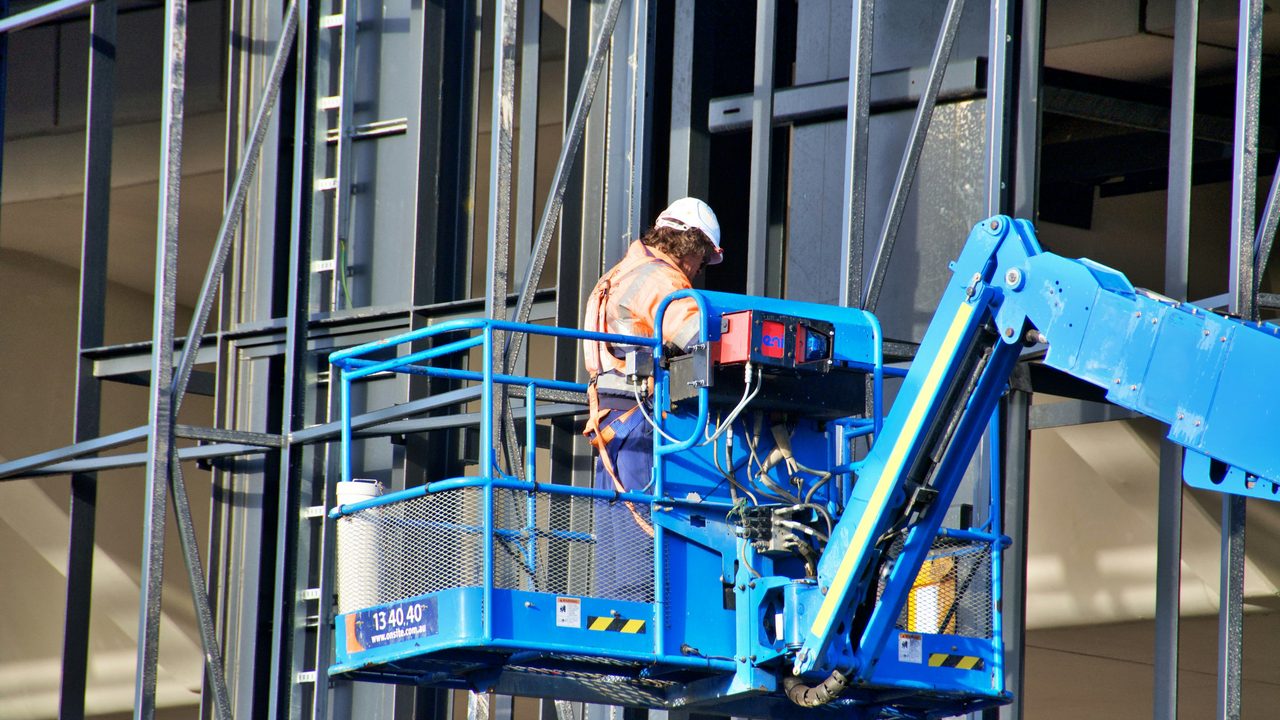 A worker in a boom lift basket working at height against a steel frame