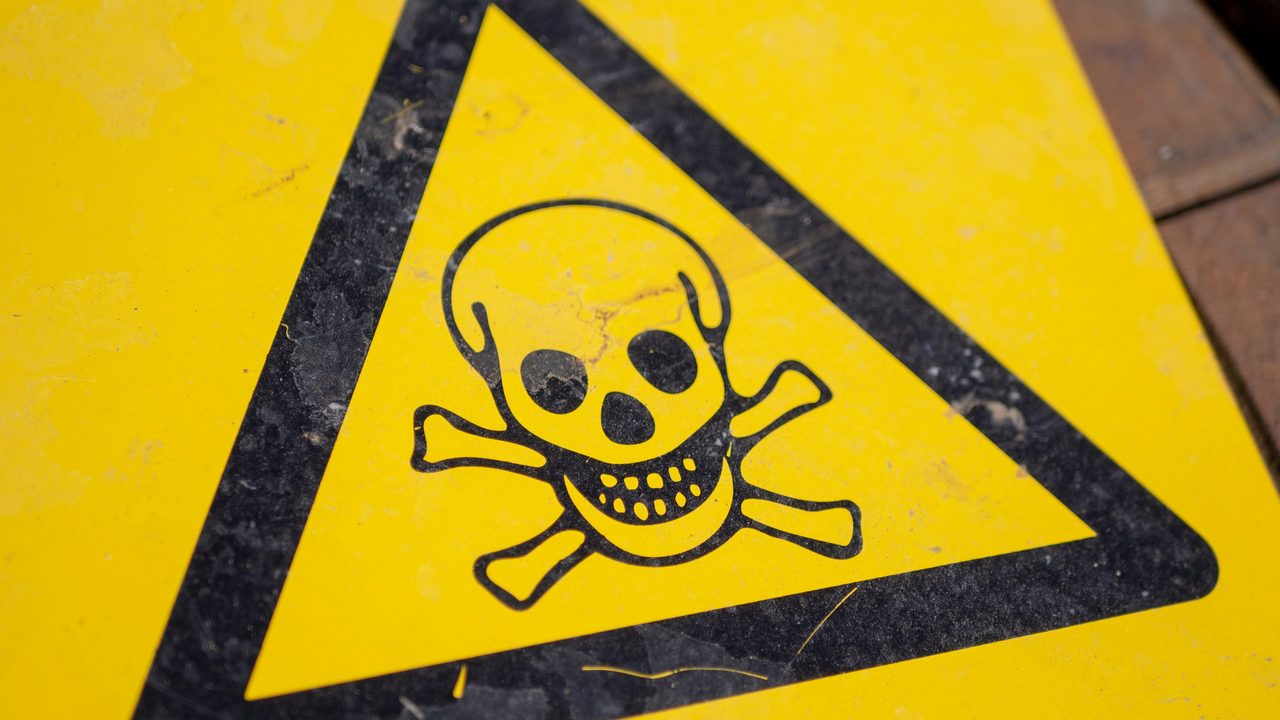 A weathered yellow hazard sign with a skull-and-crossbones toxic symbol