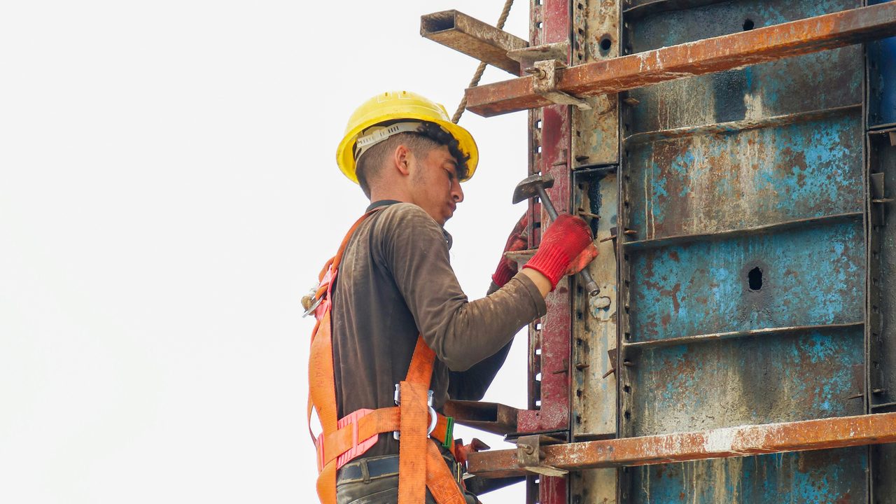 Worker in a full-body harness climbing steel formwork on a construction site